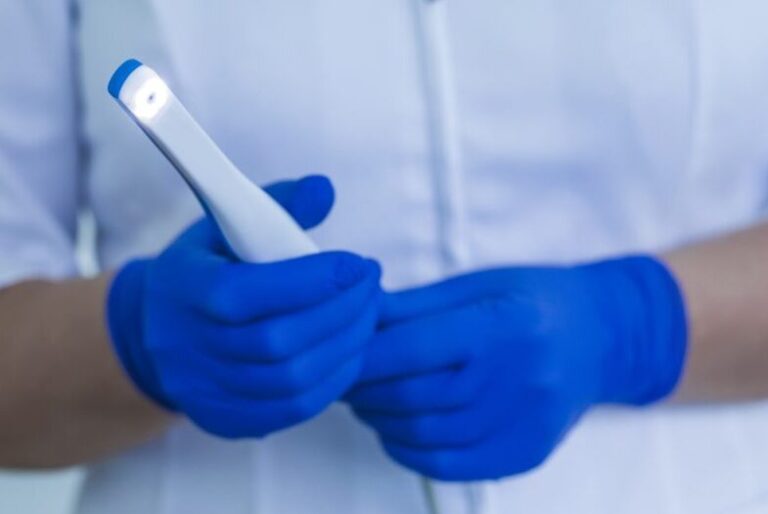 A dental assistant wearing blue medical gloves holds an intraoral camera