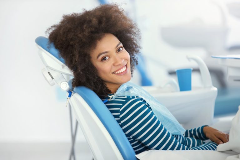 A female dental patient sits in an exam chair and smiles while looking over her shoulder
